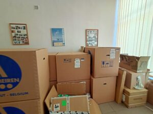 Jasny pokój w nim szereg tekturowych pudeł różnej wysokości, szerokości i grubości. Niektóre pudła stoją na innych. W polu widzenia 16 pudeł.