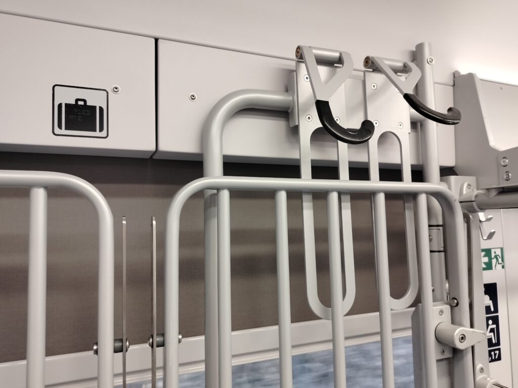 Piktogram walizki nad rozkładanymi pólkami. Widoczna górna część pólek.