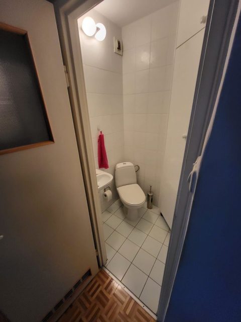 Widok na starą toaletę. W malutkim pomieszczeniu o nierównomiernym kształcie ustawiona pod katem muszla toaletowa i po jej lewej stronie malutka umywalka.